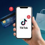 A hand holds a smartphone displaying the TikTok logo with a red warning icon. Nearby, a credit card with an exclamation mark and a transparent shopping bag are visible.