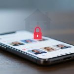 A smartphone on a wooden table displaying a social media app with profile pictures. A red padlock icon overlays the screen, symbolizing security.