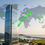 A tall glass skyscraper stands near wind turbines and solar panels, with a world map and green arrows in the background. The setting includes a coastal landscape with fields and a body of water.