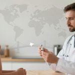 A doctor in a white coat holds a vaccine vial, showing it to a young girl with a ponytail. They are in a modern room with a world map and bridge illustration in the background.