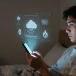 A person in a white shirt lies in bed, holding a smartphone. Holographic weather icons, including a cloud with rain, are projected above the device.