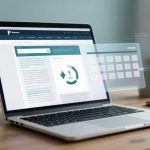 A laptop on a wooden desk displays a webpage with text and graphics. A transparent digital interface with a numeric keypad floats above. A smartphone and white mug are nearby.