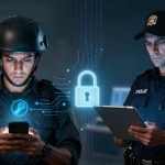 Two police officers focus on devices; one uses a smartphone, wearing a helmet, while the other holds a tablet. A digital lock graphic appears between them, symbolizing cybersecurity.