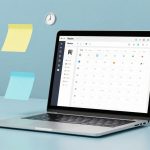 A laptop displaying a calendar app on the screen is set on a light blue surface. Floating nearby are yellow and blue sticky notes, two wall clocks, and a small red desk calendar.