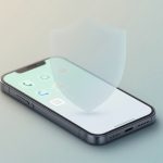 A smartphone displaying app icons on its screen with a translucent shield hovering above, symbolizing security or protection.