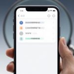 A hand holding a smartphone displaying a blurred app interface with several list items and icons. A magnifying glass is visible in the background.