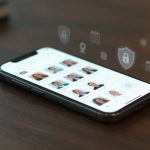 A smartphone on a wooden table displays a contact list with profile photos. Floating icons above show a lock, calendar, and location.