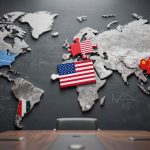 A world map on a blackboard with puzzle pieces representing different countries. The USA is marked with its flag, China with a red piece, NATO with a blue piece, and Ukraine with a blue and yellow piece. Mathematical equations are drawn on the blackboard. A conference table with chairs is in the foreground.
