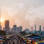 A bustling market scene with colorful stalls and numerous people walking. Skyscrapers and a sunset are in the background, with a faint world map overlay in the sky.