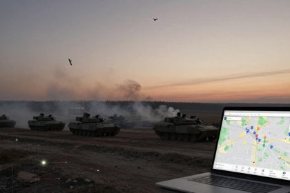 A group of tanks in a dusty field under a sunset sky with smoke rising. Two drones fly above. In the foreground, a laptop displays a map with markers.