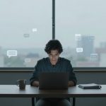 A person sits at a table using a laptop, with a mug and a notebook nearby. Speech bubbles and calendar icons float around, suggesting digital communication. A large window in the background shows an out-of-focus cityscape.