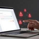 A hand pointing at a laptop screen displaying a chat interface. Red warning icons hover above the keyboard, indicating alerts.