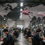 A factory floor with rows of workers at computer stations, wearing dark uniforms. A digital world map overlay displays data points.