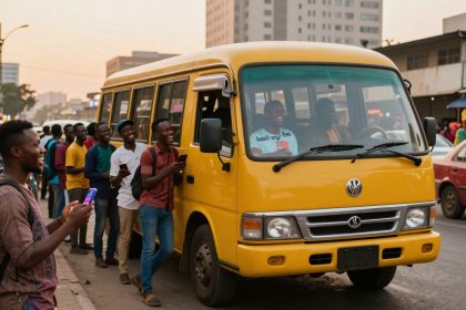 A group of people, some holding phones, stand and laugh near a yellow bus on a city street. Buildings and other vehicles are in the background.