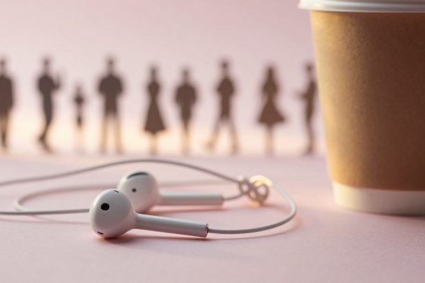 White earphones on a pink surface next to a brown paper cup. Blurred silhouettes of people are visible in the background.
